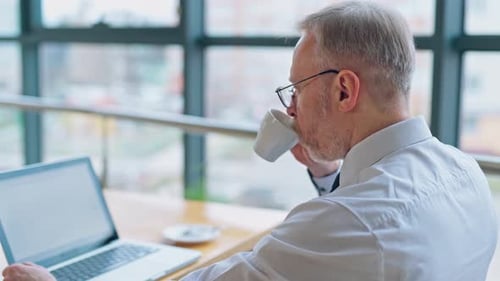 Mature Man Works on Laptop and Drinks Coffee