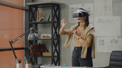 Female Engineer in the Office in a Virtual Reality Helmet Uses Gestures to Manage the Project