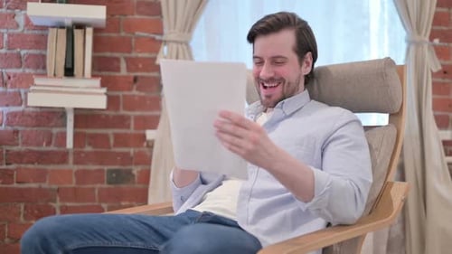 Man Sitting, Reading a Paper and Smiling