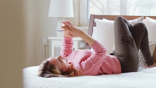 Woman Relaxing on Bed Using Smartphone