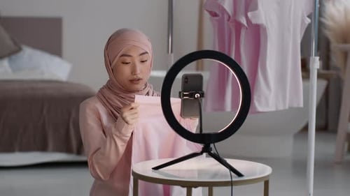 Popular Asian Lady Fashion Blogger in Hijab Recording Video Review of New Clothes Collection at Home