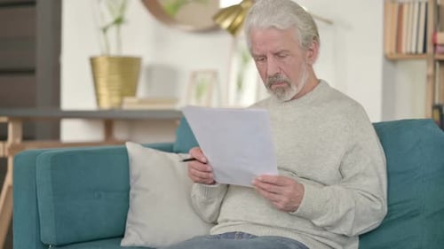 Senior Adult Reads Documents on Couch