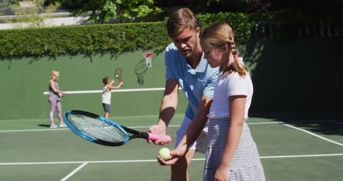 Caucasian father teaching his daughter to play tennis at tennis court on a bright sunny day