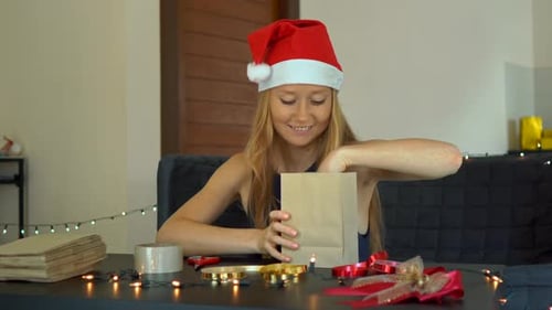 Woman Wearing Santa Hat Looks in Christmas Gift Bag