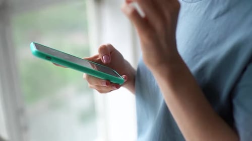 Close-up of Hands of Unrecognizable Young Woman Using Cell Phone Near Window on Sunny Bright Day.