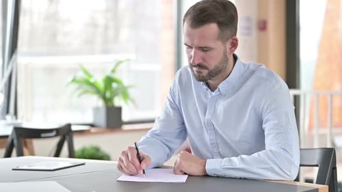 Focused Young Man Doing Paperwork in Office