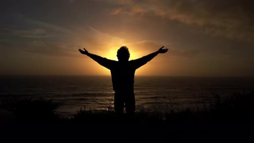 Person with Arms Raised at Sunset Above Ocean