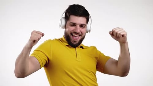 Bel homme à la barbe dansant avec des écouteurs en studio sur fond blanc
