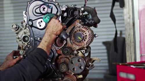 Car Mechanic Assembles Parts Of Car Engine With Cordless Screwdriver In The Repair Shop