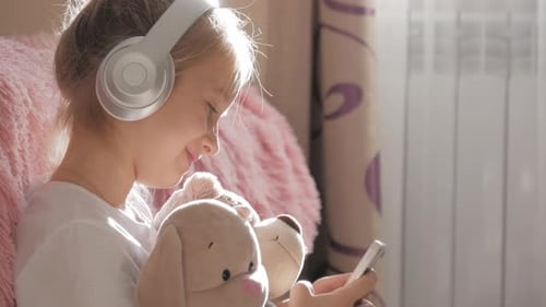 A School Girl Plays the Phone Lying on the Floor in Her Room, Along with Her Her Favorite Toys