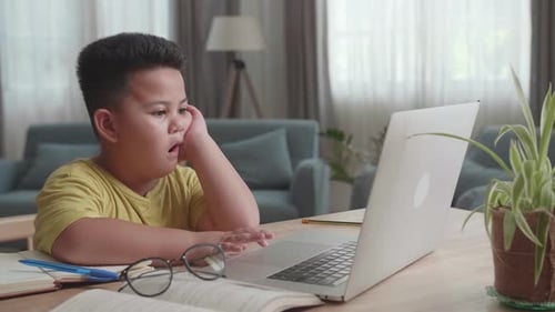 Gelangweilter asiatischer kleiner Junge benutzt Laptop im Wohnzimmer