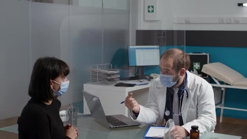 Doctor Consults with Patient in Clinic Wearing Face Masks