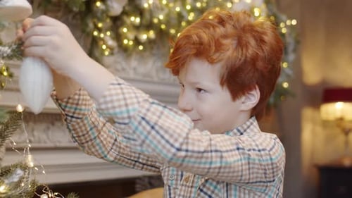 Red-Haired Boy Decorates Christmas Tree at Home