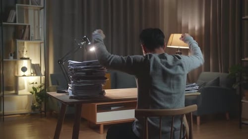 Vista posterior del feliz hombre asiático celebrando terminar de trabajar con documentos en casa