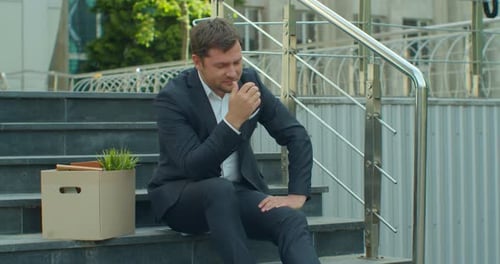 Empresario sentado en las escaleras cerca del centro de oficinas con caja de cartón y documentos con una flor de mesa