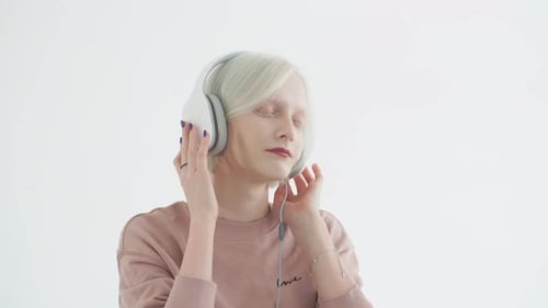 Junger Albino-Teenager hält Kopfhörer mit Händen und hört Lieblingstitel