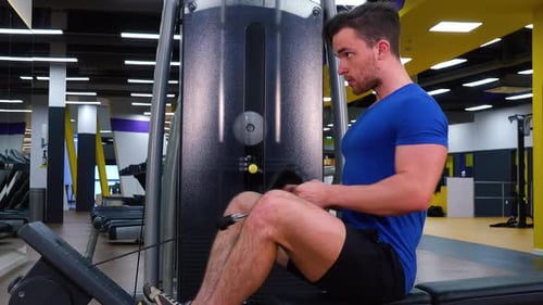 A Young Fit Man Trains on a Rowing Machine in a Gym - View From the Side