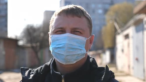 Portrait of Man with Medical Face Mask Stands at City Street During COVID19 Epidemic
