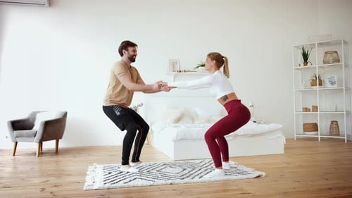Young Couple is Doing Squats Excercises at Home in Cozy Bright Bedroom Slow Motion