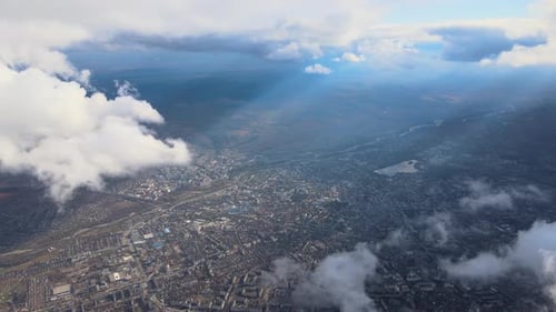 Aerial View From Airplane Window at High Altitude of Distant City Covered with Puffy Cumulus Clouds