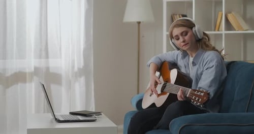 Woman Plays Guitar and Watches Laptop at Home