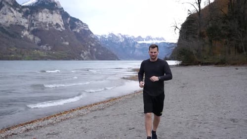 Male jogger finishes his fitness program on his smartwatch on the shore of a mountain lake