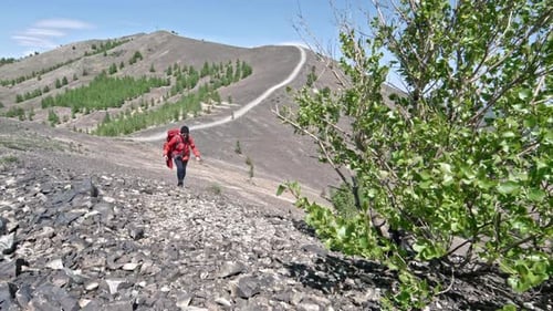 Hiker Ascends Rugged Mountain Trail on Sunny Day