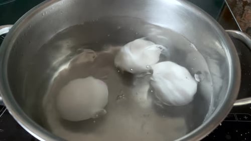 Hühnereier kochen in einer Edelstahlpfanne mit heißem Wasser kochen und die Eier sind mit m bedeckt