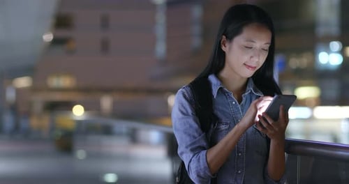 Woman watching on mobile phone in city at night