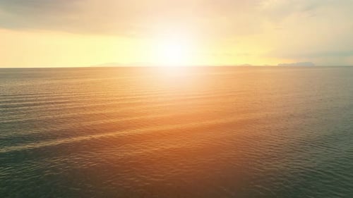 An aerial view of a drone flying over sea waves during sunrise