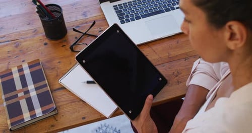 Woman Looking at Tablet at Desk With Laptop
