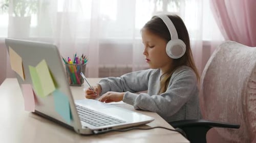 Girl Writing with Laptop and Headphones Indoors