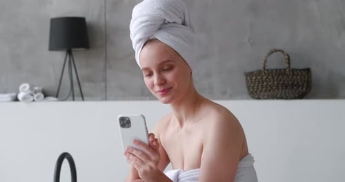 Woman in Towel Smiling, Looking at Phone