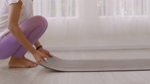 Asian woman's hands rolling up her yoga mat after a workout at the studio.