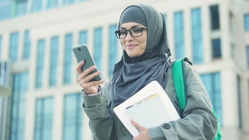 Happy Muslim Woman Student Chatting on Phone Outdoors on University Campus