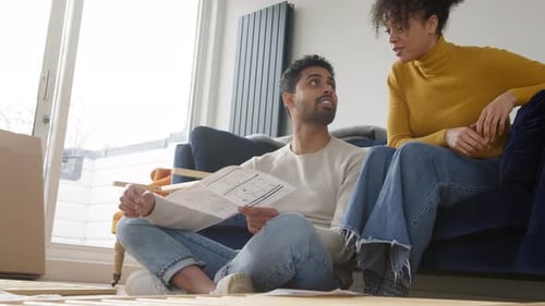 Young Couple In Lounge At Home Arguing Whilst Reading Instructions For Flat Pack Furniture Assembly
