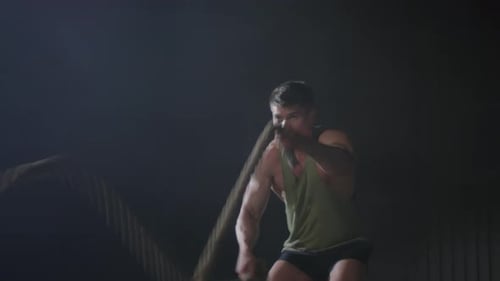 Muscular Man Training with Battle Ropes in Gym
