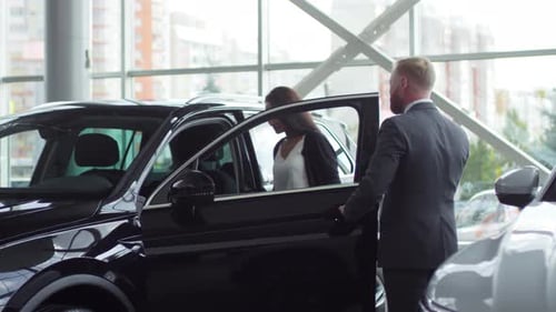 Young Attractive Woman Choosing New Car with Assistant of Salesman