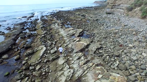 Tracking shot of a young man running on a rocky ocean beach shoreline