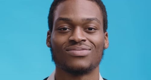 Nahaufnahme eines fröhlichen Afroamerikaners, der in die Kamera lächelt, blauer Studiohintergrund