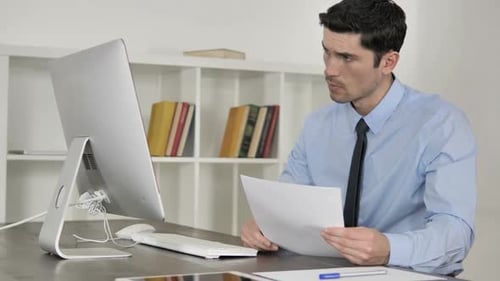 Man Reviews Documents at Modern Computer Desk