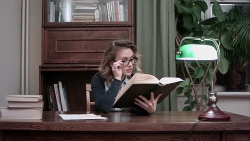 Woman Reads Thick Book at Wooden Desk