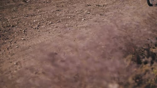 A biker rushes along a sandy track, leaving behind a cloud of dust, close-up. Slow motion.