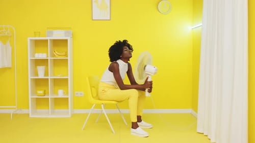 Woman Cooling Off with Fan in Yellow Room
