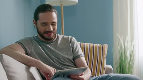 Man Uses Tablet on Couch at Home