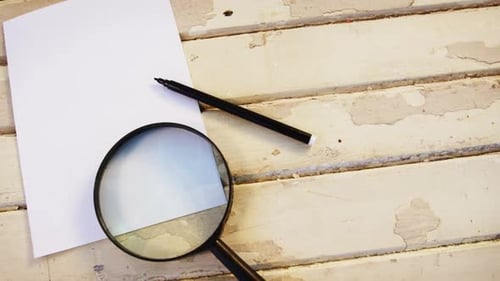 Magnifying glass, pen and paper on wooden plank