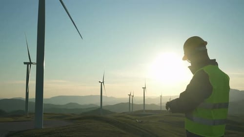 Technician Engineer in Wind Turbine Power Generator Station Standing with a Tablet in His Hands