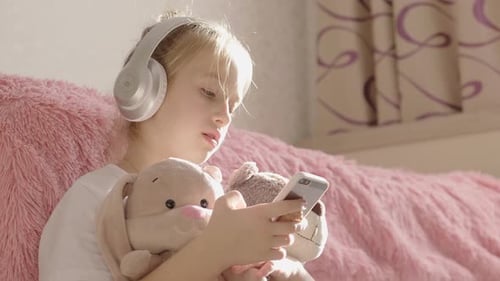 A School Girl Plays the Phone Lying on the Floor in Her Room, Along with Her Her Favorite Toys.