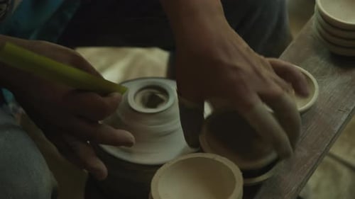 Close-up of a woman working on a potter's wheel making clay objects in pottery workshop.