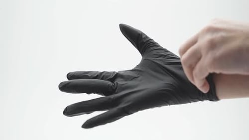 Gros plan de la main d'une femme habillant un gant médical, latex, nitrile, noir sur fond blanc